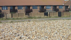 A row of brick buildings with a flat roof, a gravel driveway, and a fence.