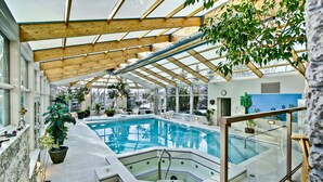 Une piscine intérieure dotée d’un toit en verre, entourée de plantes en pot et d’un mur en pierre.