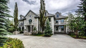 Une grande maison en pierre, dotée d’une entrée imposante, de nombreuses fenêtres et d’une allée bien entretenue.
