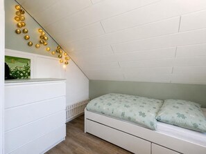 Ein Schlafzimmer mit schrägverdeckter Decke, einem Bett mit gemusterten Betttextilien, einer Kommode und Wandleuchten in Lichterkette-Optik.