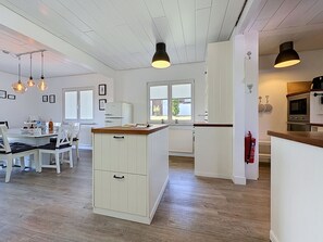 Een moderne keuken met witte kastjes, een houten aanrecht en hangende lampen. Er is een eethoek met witte stoelen en een tafel.