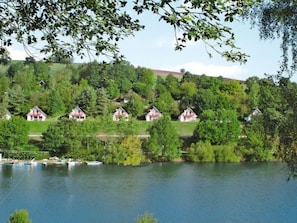 Une vue sur le lac, avec plusieurs maisons situées sur une colline, des bateaux amarrés au bord de l’eau et une végétation luxuriante.