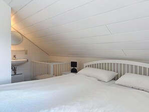 A bedroom with a sloped ceiling, a bed with white bedding, a bedside table, and a wall-mounted light fixture.