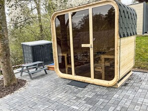 Une structure en bois dotée d’une porte et de fenêtres en verre, d’un banc et d’un abri de jardin, le tout intégré dans un cadre verdoyant.