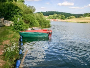 Une rivière paisible, avec un bateau vert amarré sur la rive gauche, entourée d’une végétation luxuriante et d’arbres.