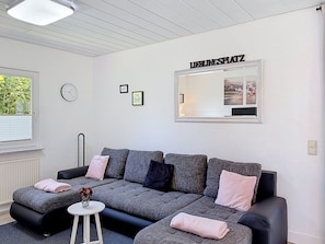 Un salon moderne avec un canapé gris, une petite table blanche, une horloge et un miroir au mur.