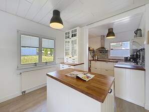 Een keuken met witte kastjes, een houten aanrecht en een raam met jaloezieën.