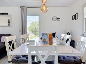Un espace repas avec une table blanche, des chaises et une vue sur l’extérieur.