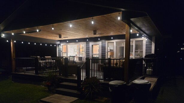 A covered porch with string lights, outdoor furniture, and a small step leading to the entrance.