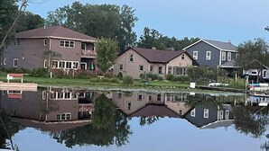 A lakeside residential area with multiple houses, a dock, and a clear reflection in the water.