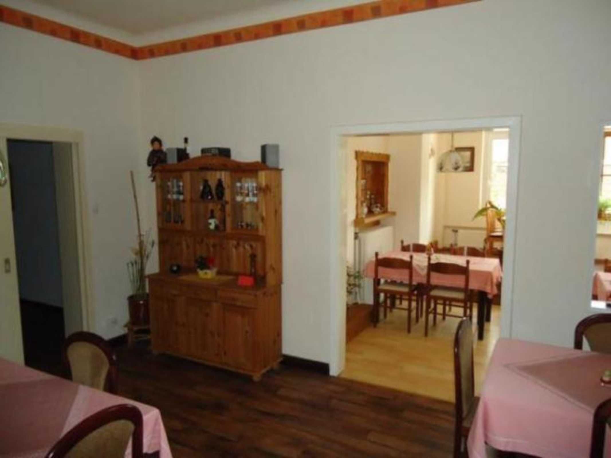 Un comedor con mesas y sillas de madera, un armario de madera con puertas de cristal y una puerta que conduce a otra habitación.