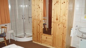A bathroom with a shower, toilet, sink, and a wooden wardrobe.