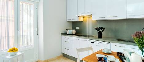 Una cocina moderna con armarios blancos, una campana extractora de acero inoxidable y un comedor con mesa y sillas de madera.