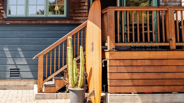 Una casa de dos pisos con un balcón de madera, una escalera y una planta de cactus en maceta.