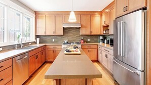 Una cocina moderna con armarios de madera, un refrigerador de acero inoxidable y una isla central con una copa de vino y fruta.