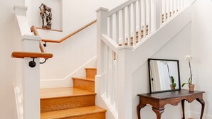 Una escalera con escalones de madera y barandillas blancas, una pequeña mesa con un cuadro enmarcado y una planta en maceta.