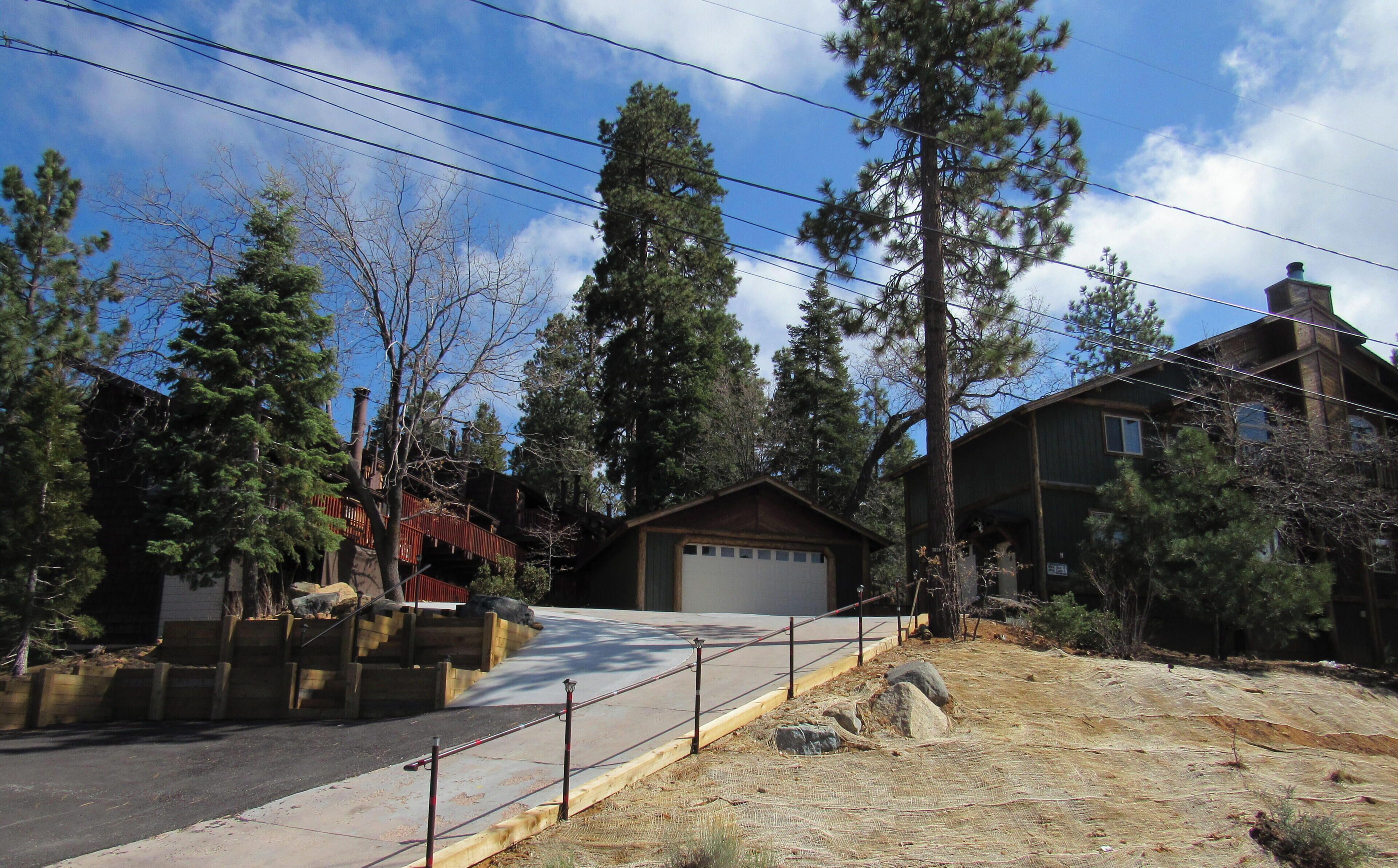 A residential area with a house, a garage, and a driveway. There are trees and a clear sky.