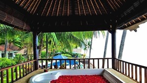 A covered outdoor area with a hot tub filled with red rose petals, surrounded by a wooden deck and a railing.