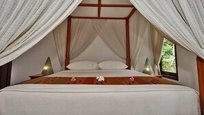 A four-poster bed with white linens and a floral bedspread, surrounded by sheer curtains.