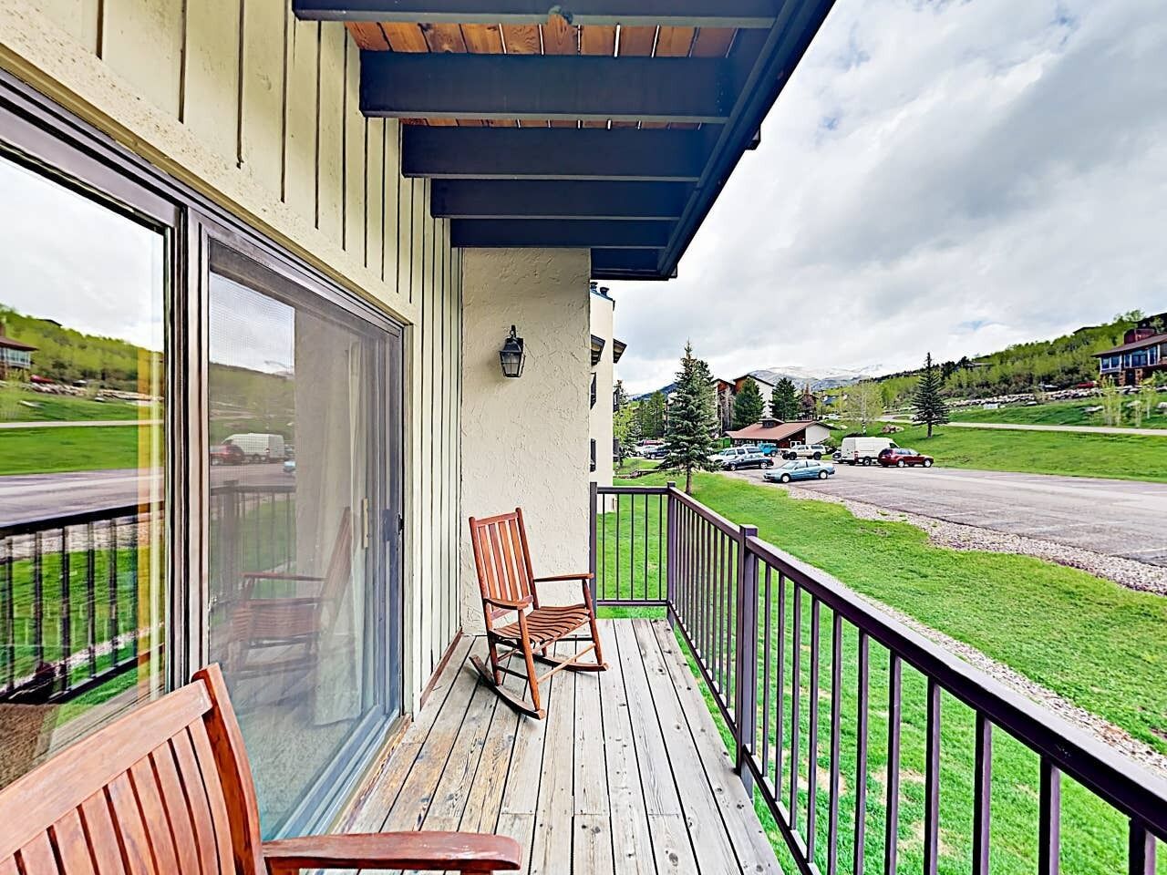 A wooden deck with a rocking chair and a bench, overlooking a road with cars and a green landscape.