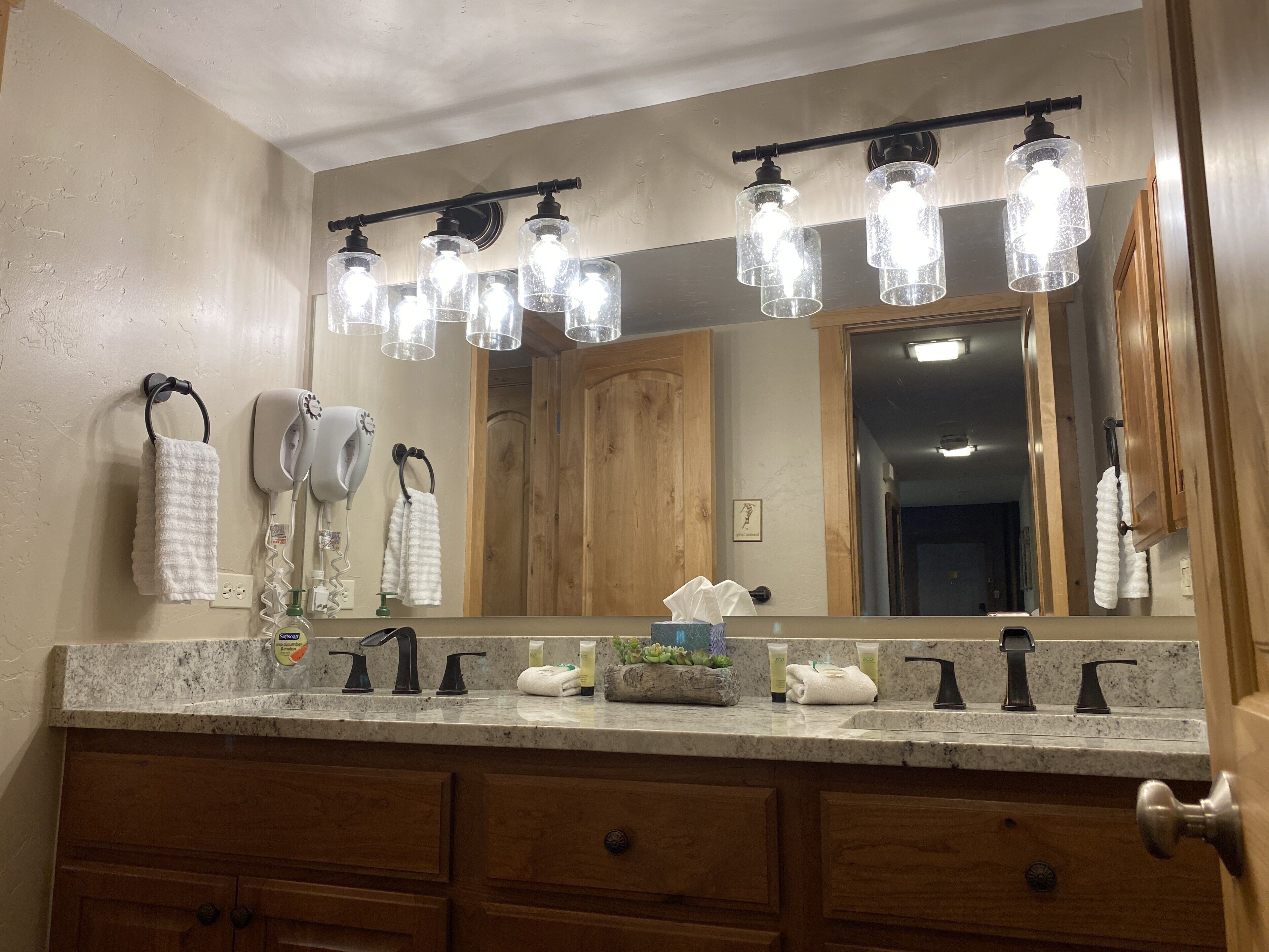 A bathroom with a large mirror, multiple light fixtures, a hairdryer, and a sink with toiletries.