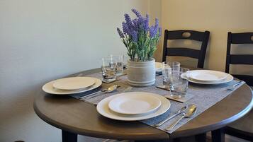 A round dining table set with white plates, clear glasses, and silverware, accompanied by a potted lavender plant.