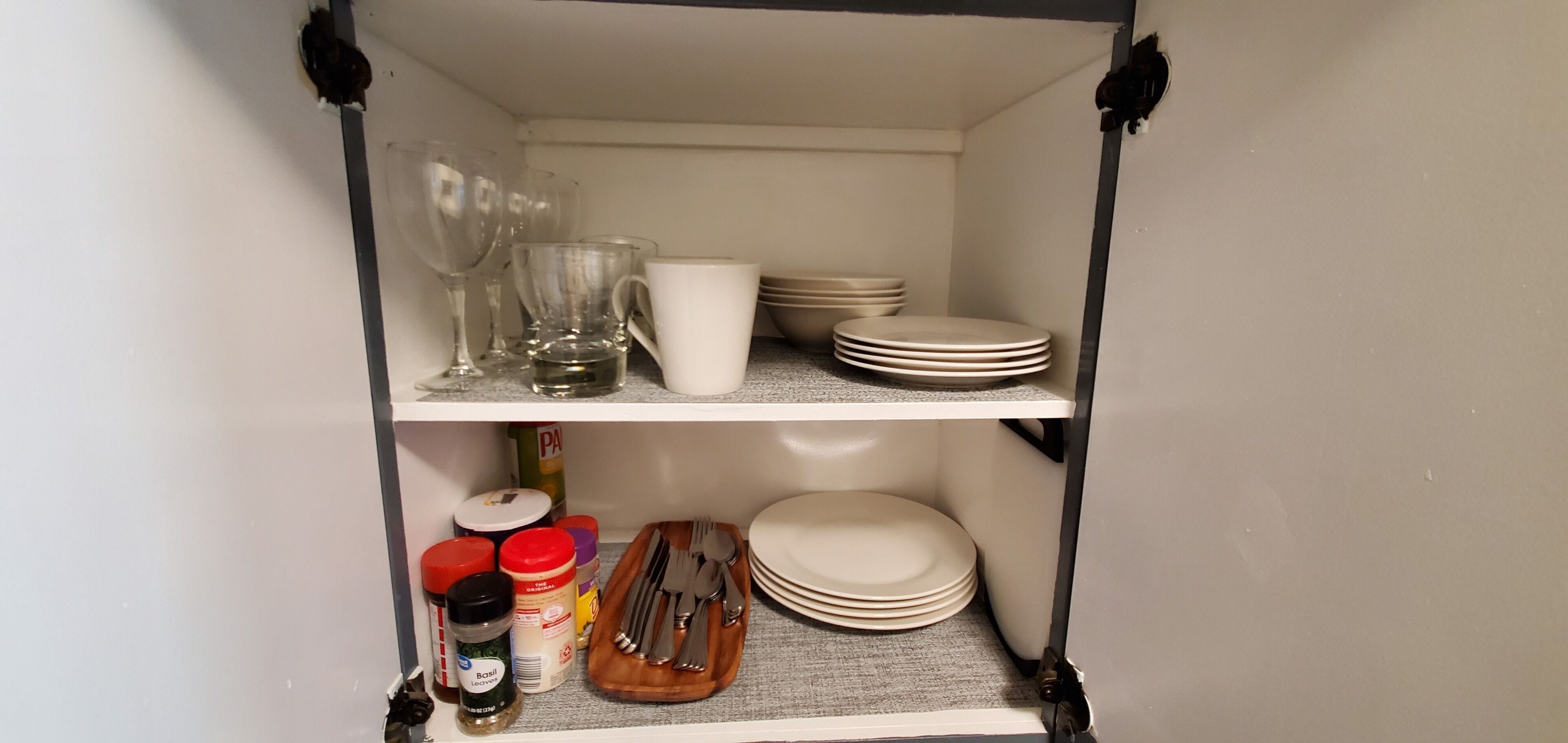 A kitchen pantry with shelves containing glassware, plates, bowls, and utensils.