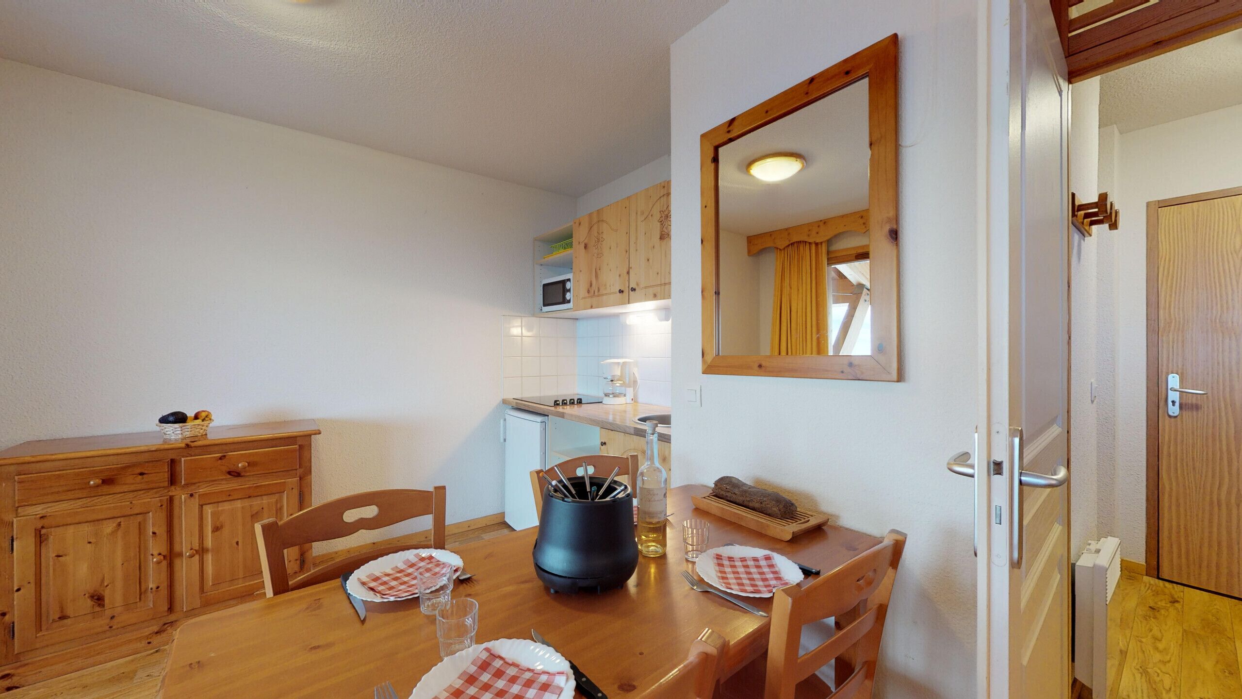 A compact kitchen with wooden cabinets, a dining table set for two, and a microwave above the stove.