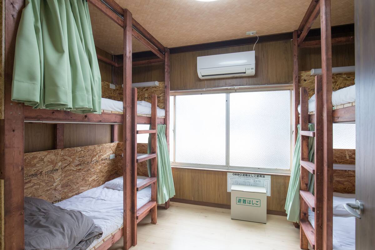 A dormitory room with bunk beds, an air conditioning unit, and a window with a view.