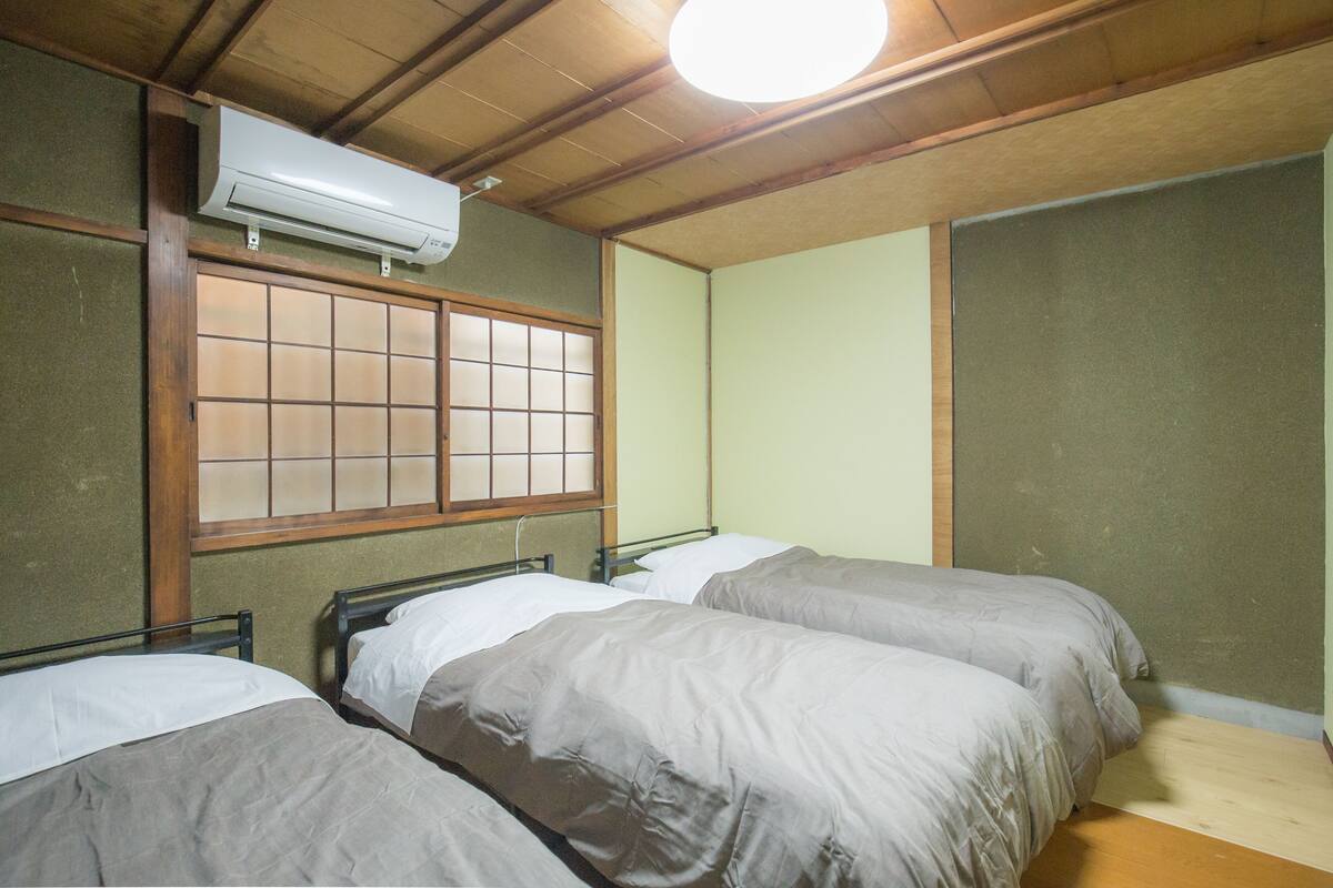 A room with two beds, a window with wooden frames, and an air conditioning unit on the ceiling.