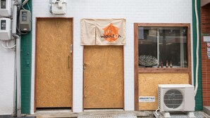 A building with three wooden doors, a banner with a logo, and an air conditioning unit outside. - Woodon - Hostel (Osaka)