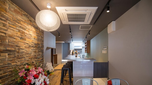 A modern kitchen with a central island, stone wall, and a floral arrangement. - Woodon - Hostel (Osaka)