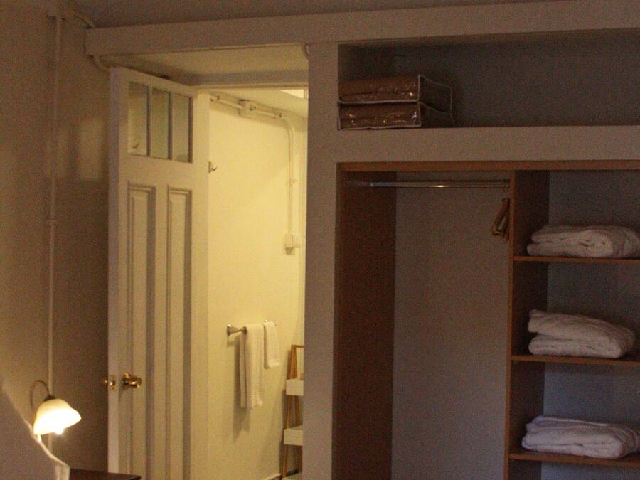 A hotel room with a bed, a bedside lamp, a wardrobe with shelves, and a door leading to a bathroom.