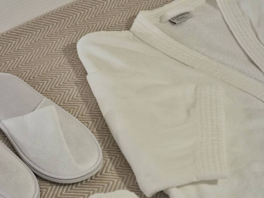 Una cama bien arreglada con una colcha estampada, un par de pantuflas blancas y una toalla blanca doblada.