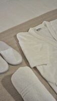 A neatly arranged bed with a patterned bedspread, a pair of white slippers, and a folded white towel.