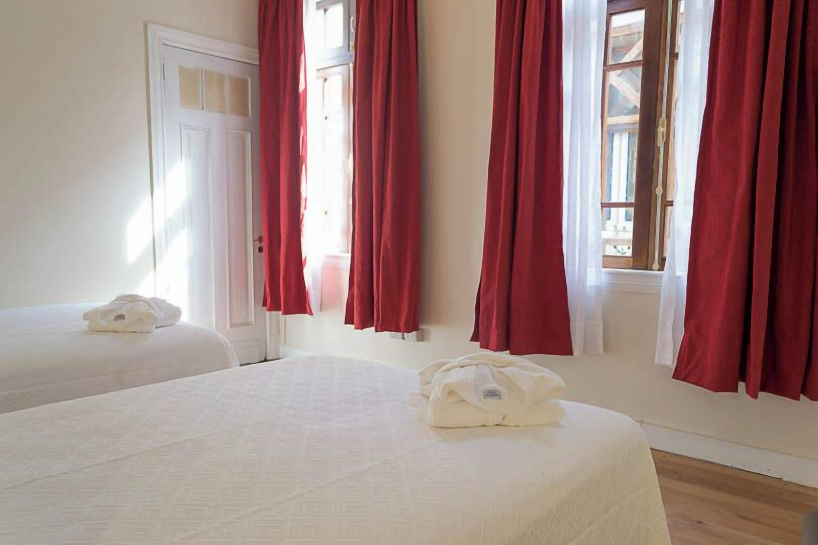 Habitació d'hotel amb dos llits, cortines vermelles i una porta blanca.