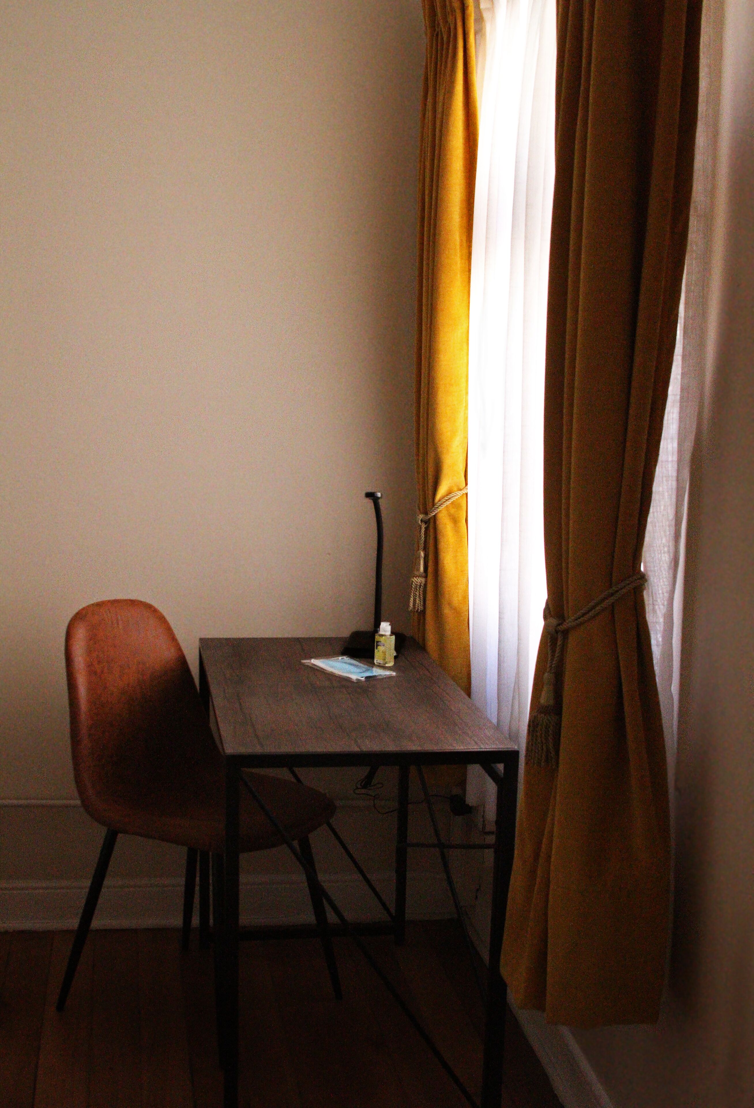 Una habitación pequeña con una mesa de madera, una silla y una ventana con cortinas amarillas.