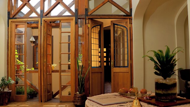 Una habitación acogedora con puertas de madera, una mesa con un libro, una planta en maceta y un recipiente de vidrio decorativo.
