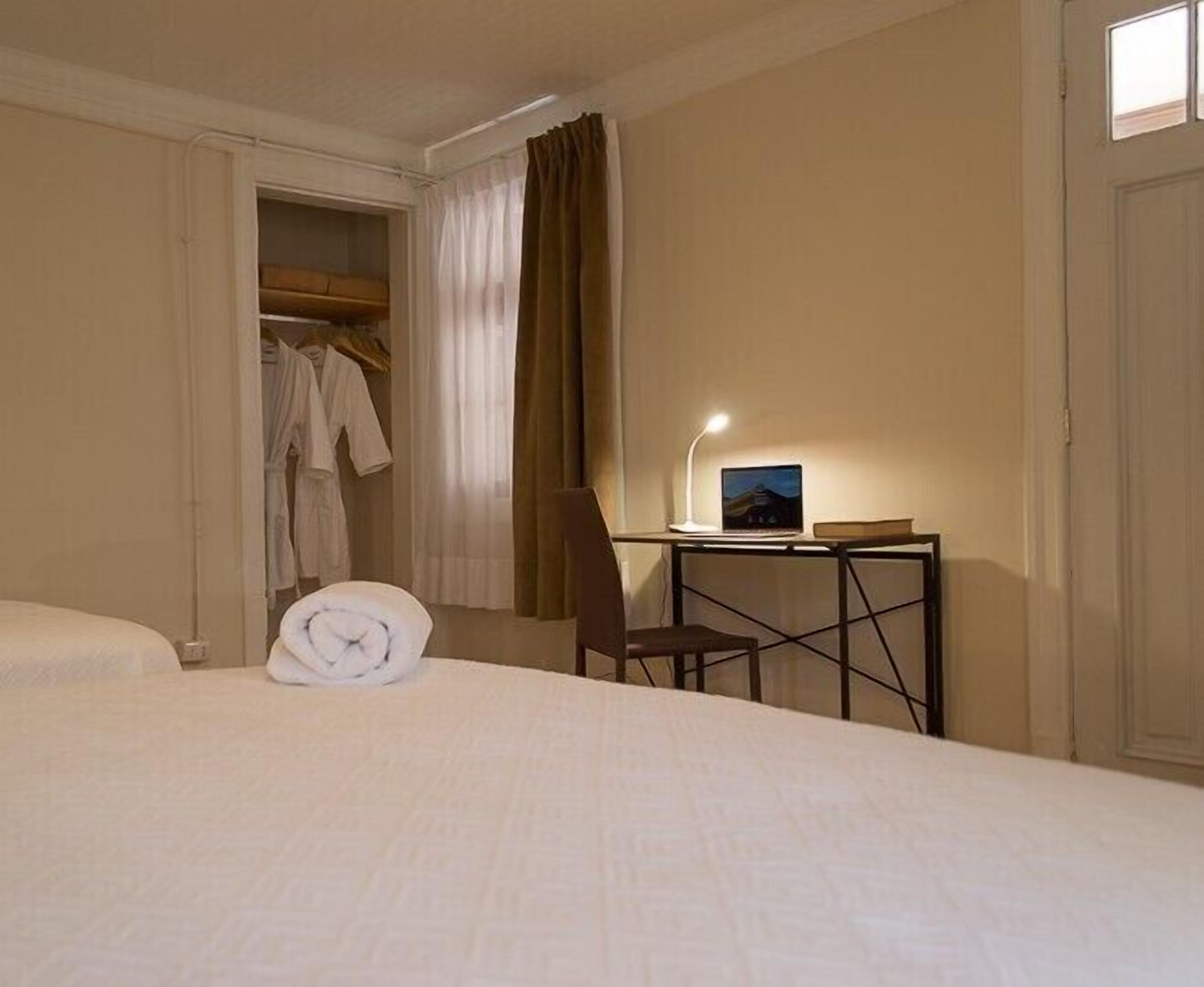 Une chambre d’hôtel avec un lit, un bureau avec un ordinateur portable, une chaise et une armoire remplie de vêtements.