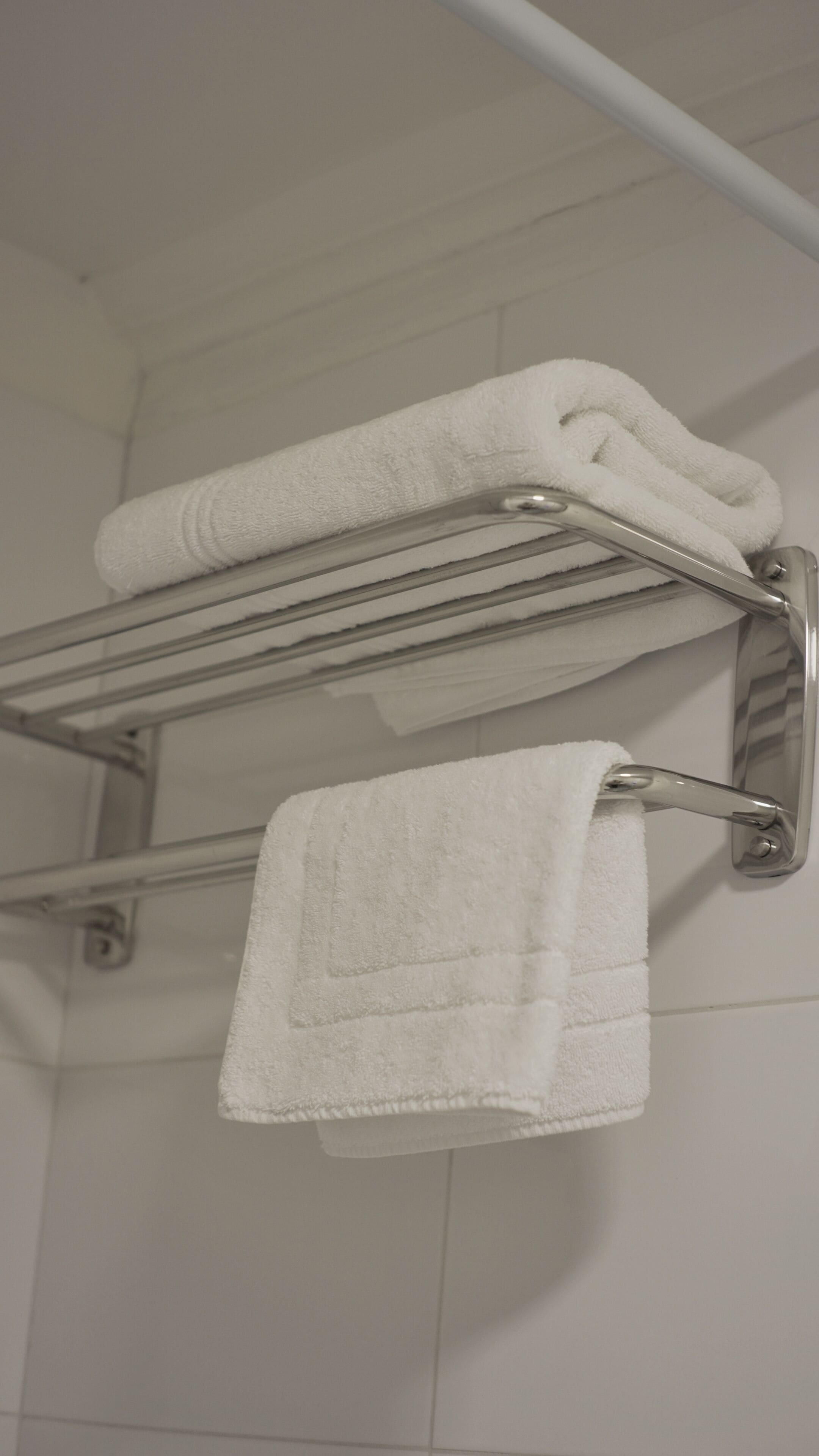 A bathroom with a towel rack holding two folded towels and a single towel hanging from the rack.