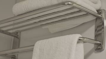 A bathroom with a towel rack holding two folded towels and a single towel hanging from the rack.