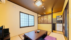 A traditional Japanese-style room with tatami flooring, a low table with a tea set, a television on a stand, and a sliding door leading to a kitchen area. - Yadoya Asakusa Sen no Kaze (Tokyo)
