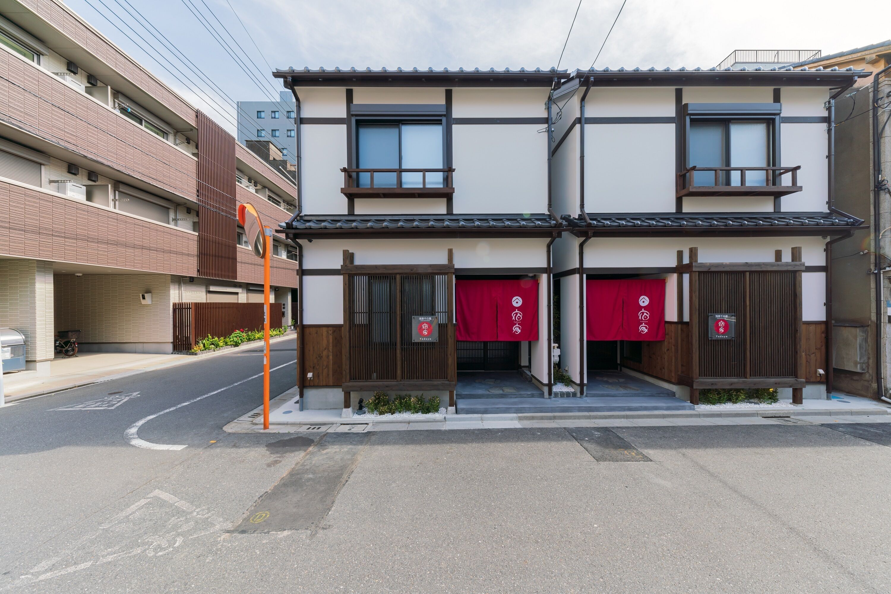Un edificio de dos pisos con arquitectura japonesa tradicional, que presenta balcones de madera y un toldo rojo.