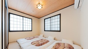 A room with tatami mat flooring, a bed with a patterned bedspread, and two windows with black frames. - Yadoya Asakusa Sen no Kaze (Tokyo)