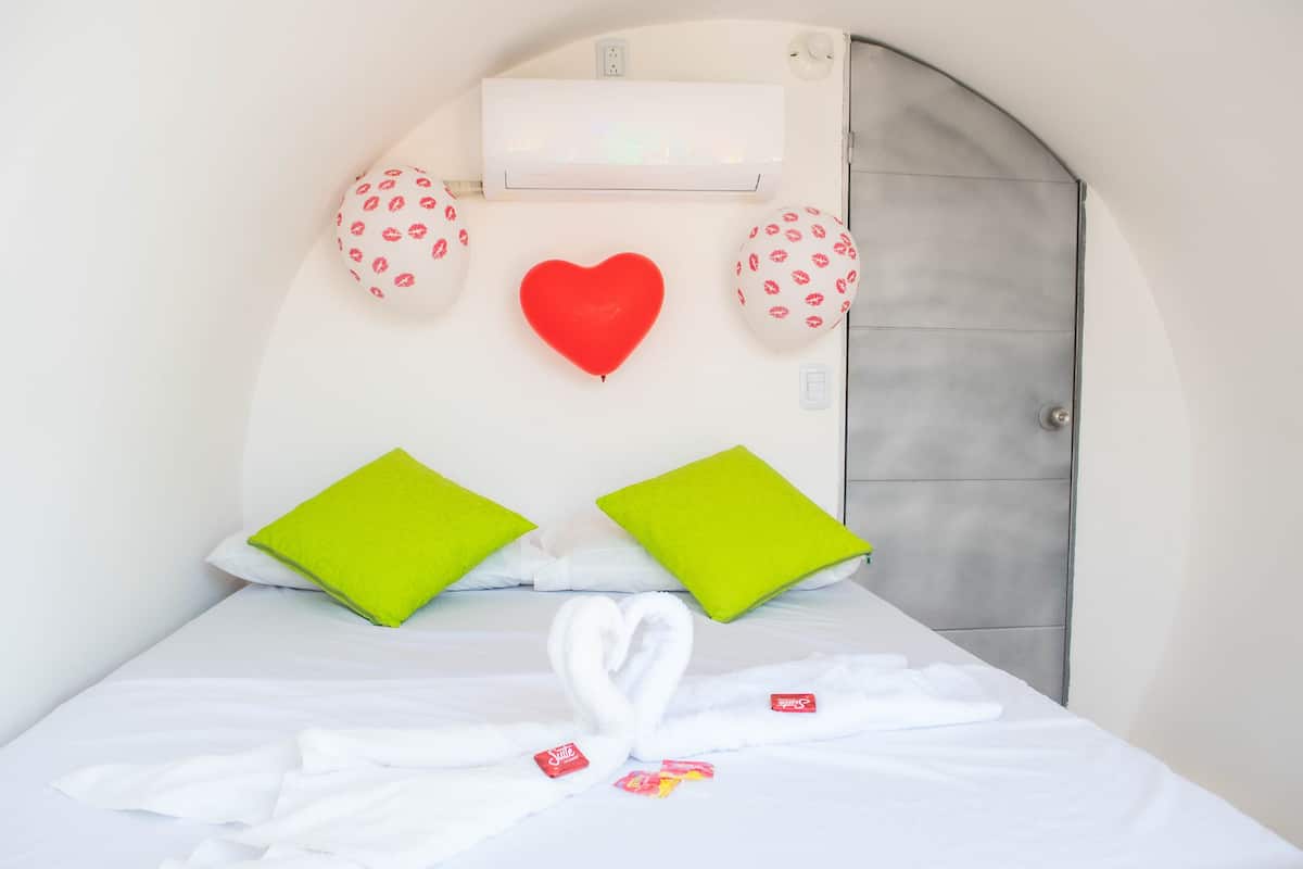A hotel room with a bed, a heart-shaped decoration, and two green pillows.