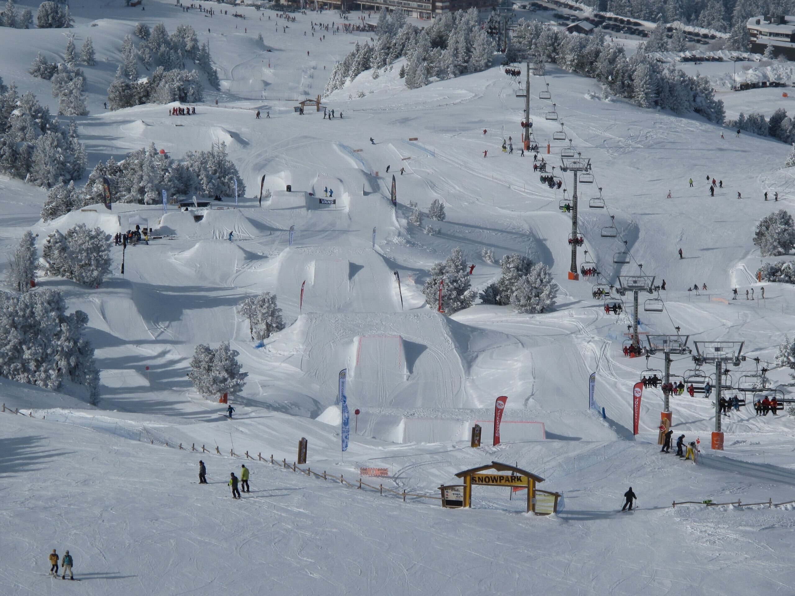 A snow-covered ski slope with ski lifts, trees, and a sign that reads "SNOWPARK".
