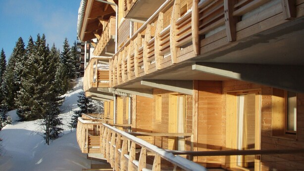 Un chalet en bois doté de plusieurs balcons, avec un sol recouvert de neige et un ciel dégagé.