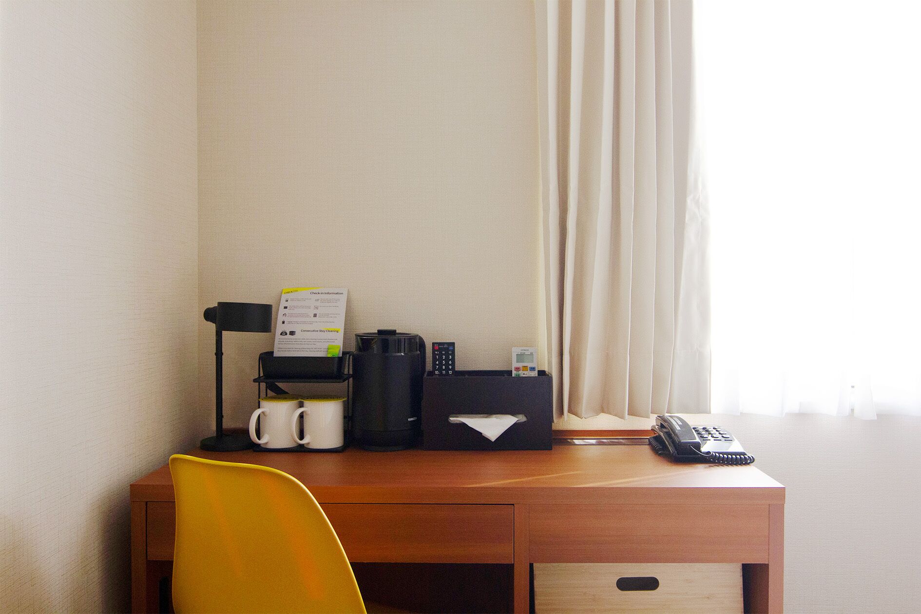 A hotel desk with a coffee maker, mugs, a telephone, and a check-in information sign.