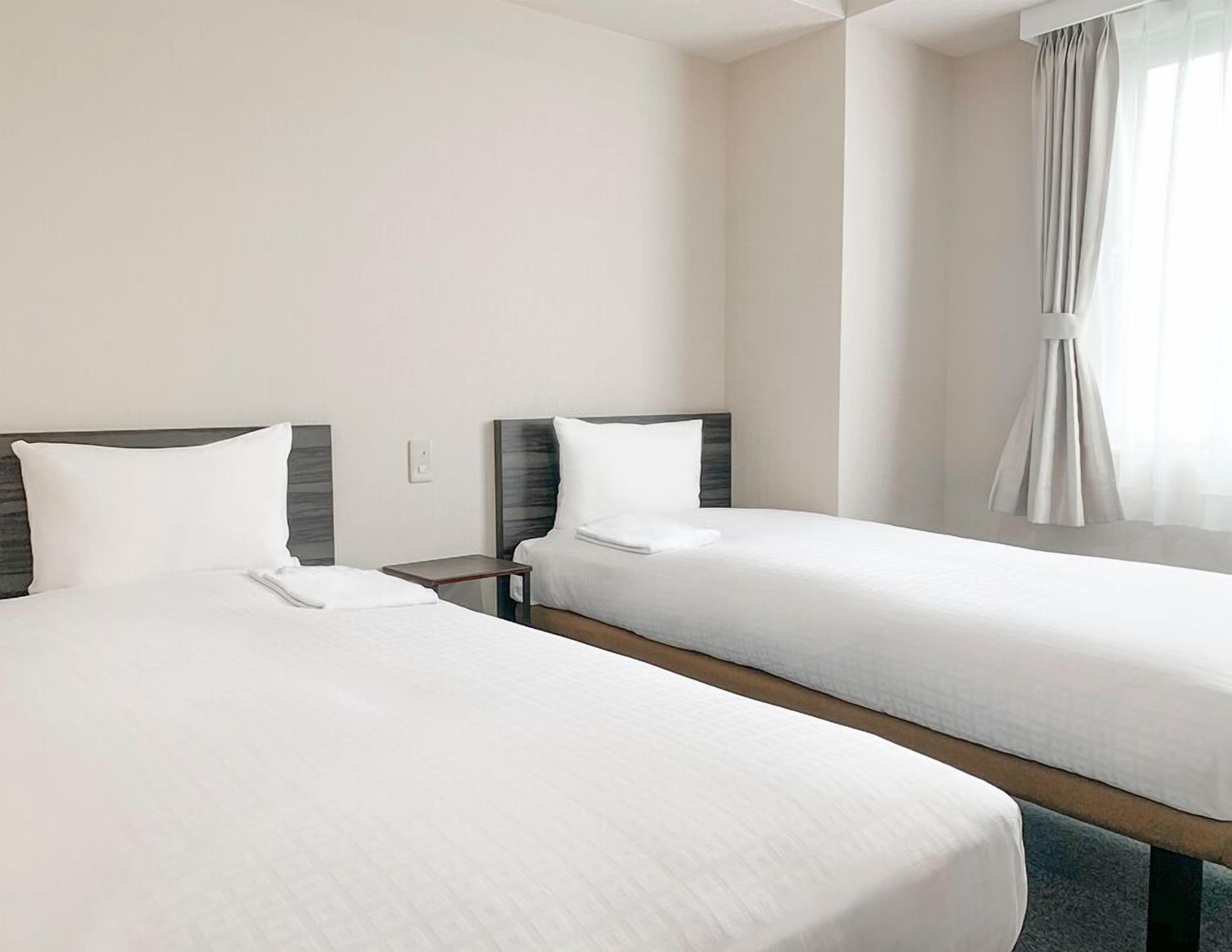Two single beds with wooden headboards, a small bedside table, and a window with curtains.