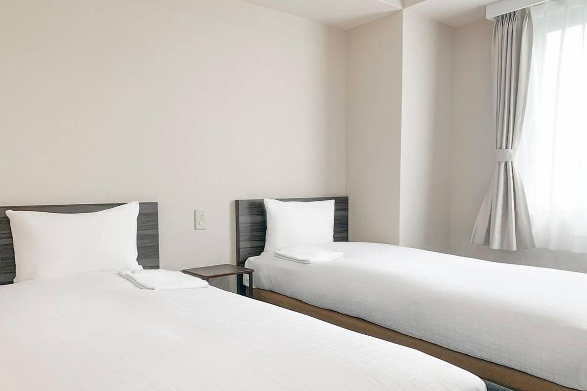 Two single beds with wooden headboards, a small bedside table, and a window with curtains.